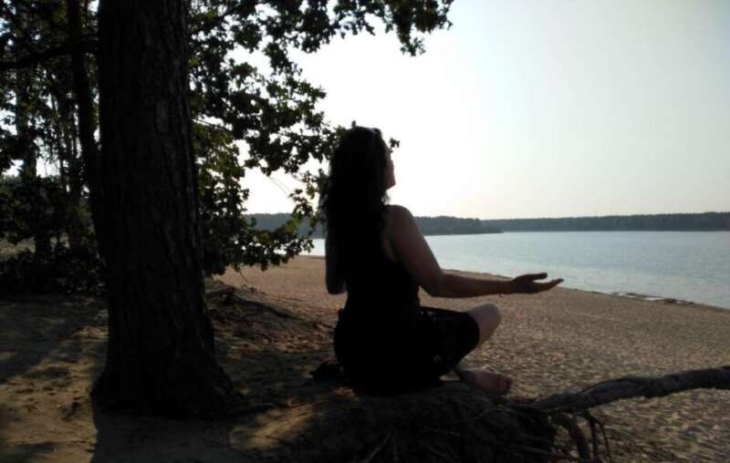 Frau meditiert am Seeufer im Schatten eines Baumes, Symbol für Lern- und Leistungssteigerung durch Hypnose. und Meditation