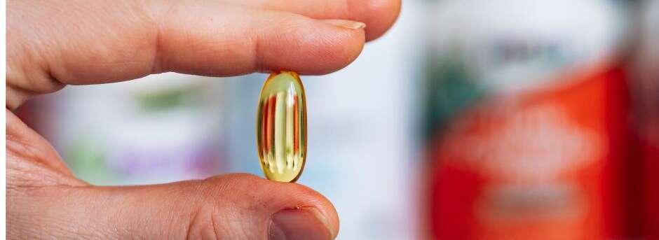 Hand hält eine gelbe Gelkapsel als Symbol für Hypno-Pharmakologie und Placebo-Wirkung